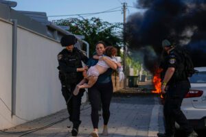 Israeli police officers evacuate a woman and a child from a site hit by a rocket fired from the Gaza Strip, in Ashkelon, southern Israel, Saturday 7 October 2023. Photo: AP Photo/Tsafrir Abayov