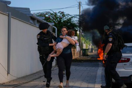 Israeli police officers evacuate a woman and a child from a site hit by a rocket fired from the Gaza Strip, in Ashkelon, southern Israel, Saturday 7 October 2023. Photo: AP Photo/Tsafrir Abayov