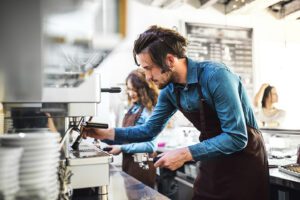 Two young baristas working in coffee shop, standing by counter, preparing coffee in machine.