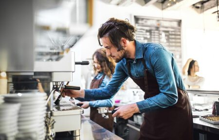 Two young baristas working in coffee shop, standing by counter, preparing coffee in machine.